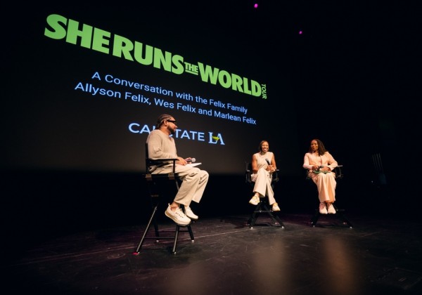 Panel discussion on stage featuring speakers seated under a “She Runs the World” presentation at Cal State LA.