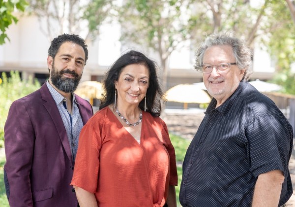 Three individuals stand outdoors on campus, posing together beneath trees during a visit to Cal State LA. 