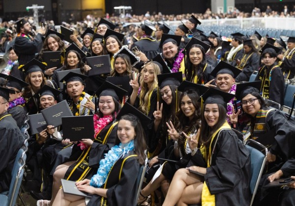 Cal State LA graduates smile, pose with diplomas, and flash peace signs during the 2025 commencement ceremony.