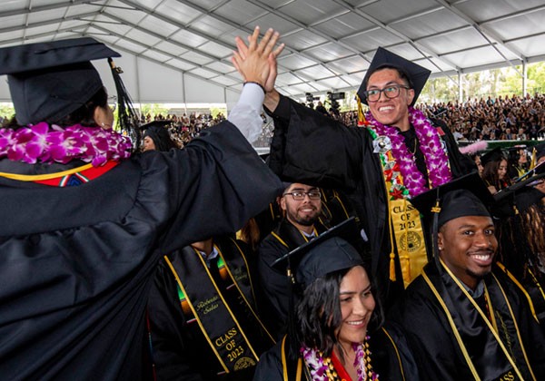 Students at graduation ceremony give each other high-fives.