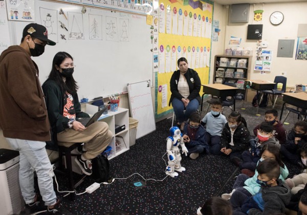 A small humanoid robot performs in front of a students in a classroom.