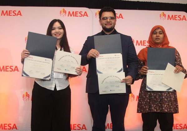 three students stand with certificate in front of MESA banner smiling