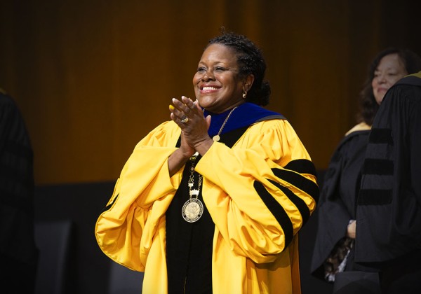 Speaker wearing a yellow jacket delivers remarks at a podium on stage during a Cal State LA event.