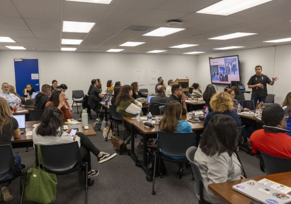 A room of people listening to a speaker give a presentation.