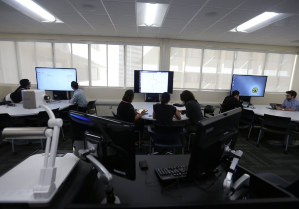 Students collaborate in a modern computer lab at Cal State LA, working at curved desks with large digital screens along a windowed wall.