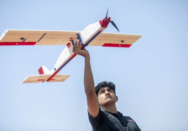 Cal State LA student holds a model UAV above their head, preparing for a flight test under a clear sky.