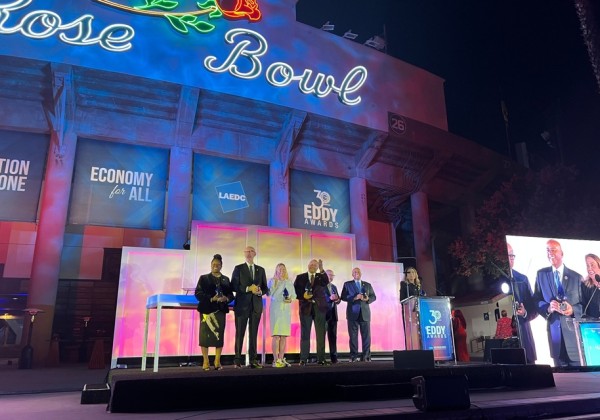 Award recipients stand on stage at the Rose Bowl during the 30th Eddy Awards, with the illuminated Rose Bowl sign and LAEDC banners in the background.