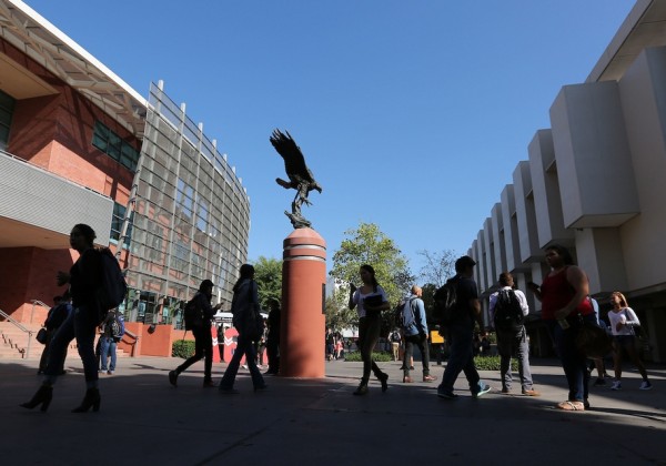 Students walk across campus beneath the Golden Eagle statue at Cal State LA, with modern buildings and a clear blue sky overhead.