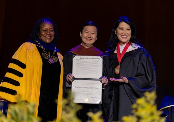 Three individuals stand on stage during a formal recognition ceremony, holding an official proclamation and smiling for the audience.