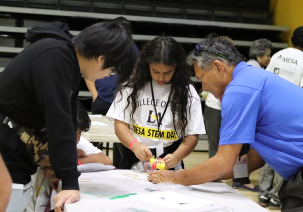 A student works on a small wheeled device with two adults during MESA STEM Day at Cal State LA.
