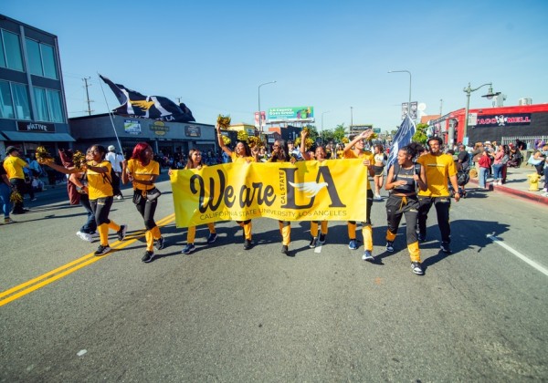 Cal State LA representatives ride in a convertible and wave to the crowd during the MLK Day Parade, carrying black-and-gold pom-poms.