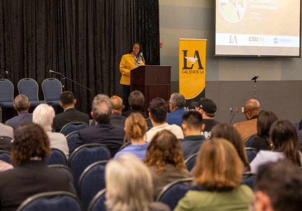 Cal State LA President Berenecea Johnson Eanes speaks at a podium during the LAEDC event, with the university banner displayed beside her.