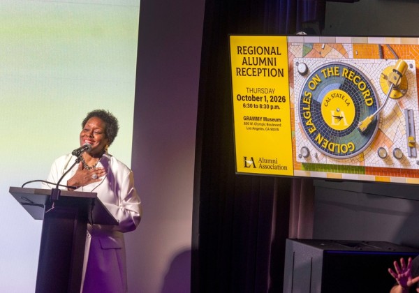 Speaker delivers remarks beside a screen displaying information for Cal State LA’s 2026 Regional Alumni Reception at the GRAMMY Museum.