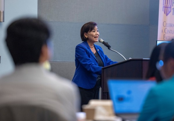 Speaker in a blue blazer delivers remarks at a podium during an event at Cal State LA, with audience members in the foreground.