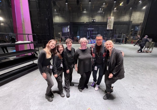 Six production team members pose together backstage in a theater.