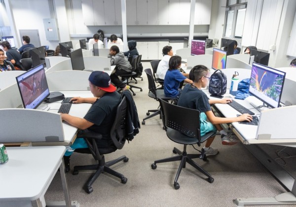 Middle school students participate in a Verizon STEM Summer Camp activity at Cal State LA, working on digital projects at desktop computers in a modern computer lab.