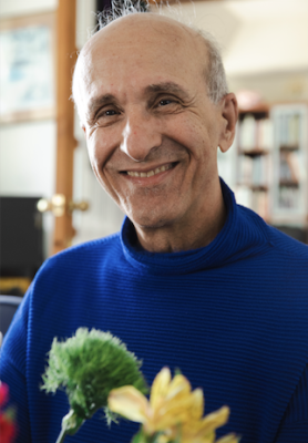 Kamran wearing indigo color turtle neck, smiling, with a yellow flower in the foreground