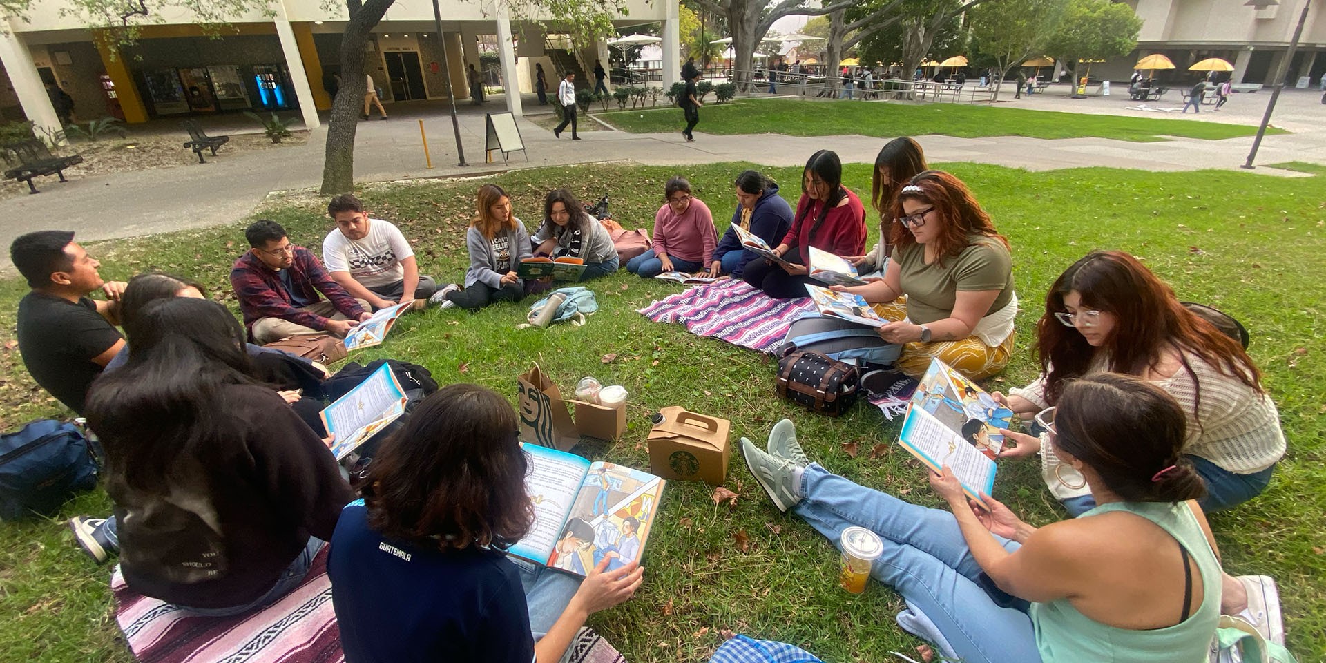 students having class on lawn area, sitting in circle and reading books