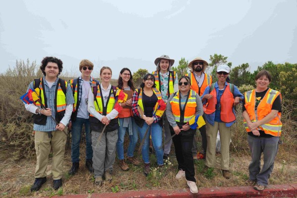 Group wearing safety vests smiling in front of the coastline.