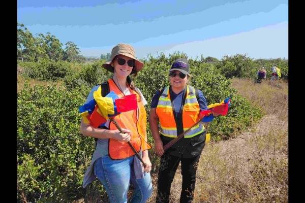 Two students wearing hats holding red and yellow flags smiling for the camera in the field.