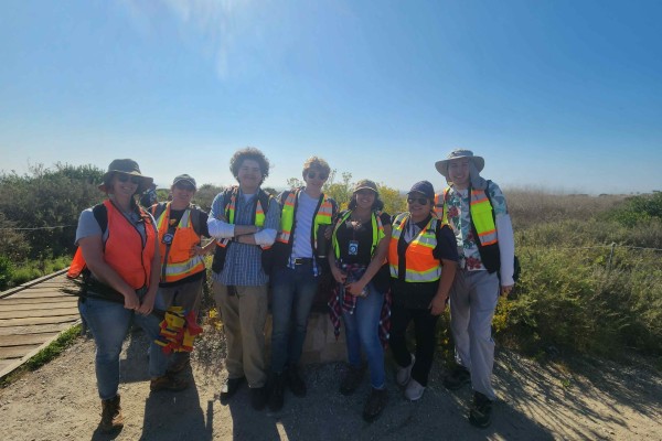 Group of students wearing safety vests and hats in front of the coast on a sunny day.