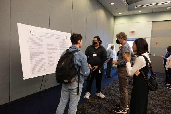 Student with cane presenting research poster to three listeners