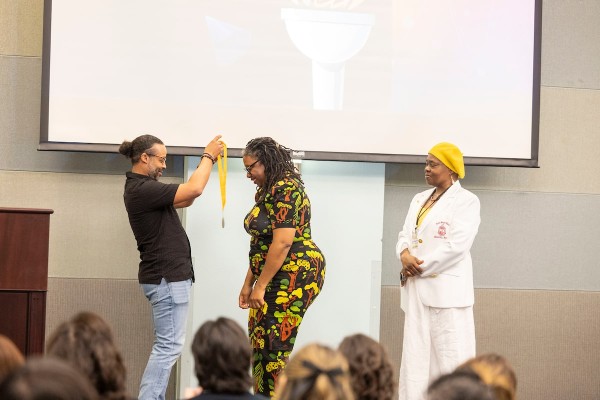 Male thesis mentor donning medal onto female student in a black dress with sunflowers