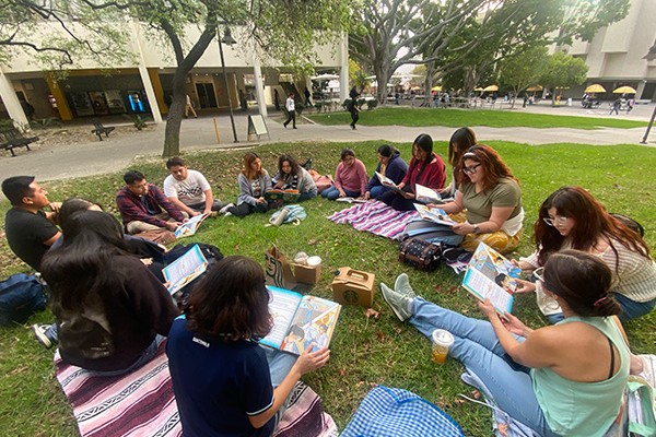 students having class on lawn area, sitting in circle and reading books