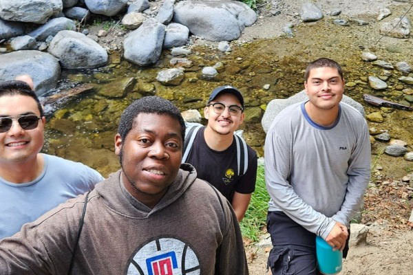5 Men smiling in front of a stream of water and boulders.