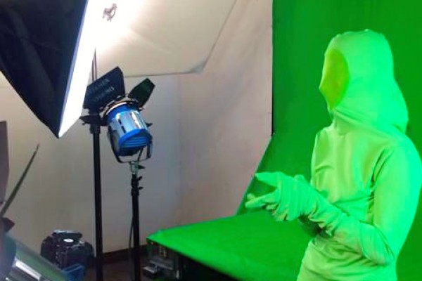 Image of a student in a green suit in front of a green screen being filmed. 