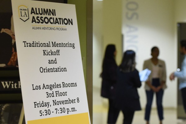 Sign for mentoring orientation with a group of people chatting in the background