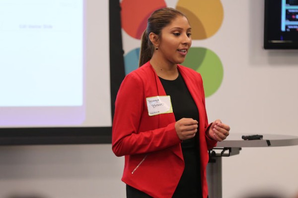 Image of a female student in a red blazer giving a presentation to her classmates. 