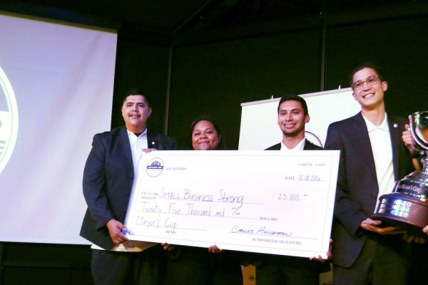Group of Cal State LA students in business attire on a stage holding a large check near a screen that says "2016 Mayor's Cup"