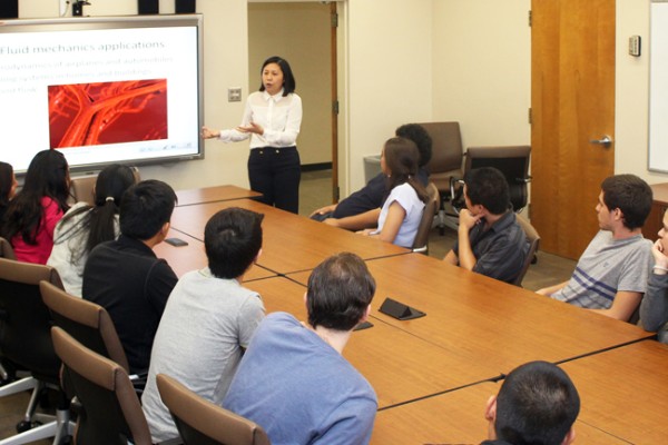 Group of Cal State LA students in a classroom around a conference table facing a projector screen as a lecturer teaches.