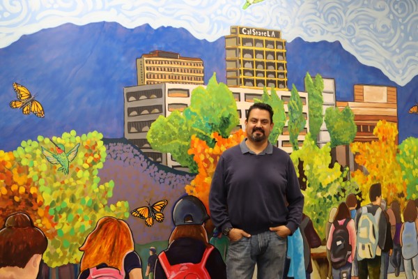 MA Student, Reynaldo Mora posing in front of a mural he painted 