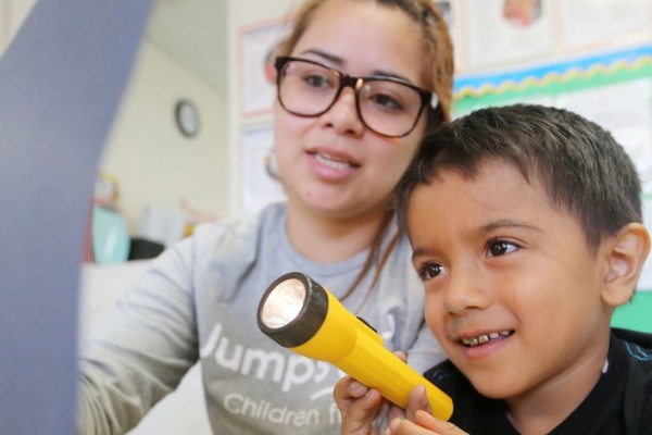 Image of a female student holding up a page for a child who is shining a flashlight on it. 