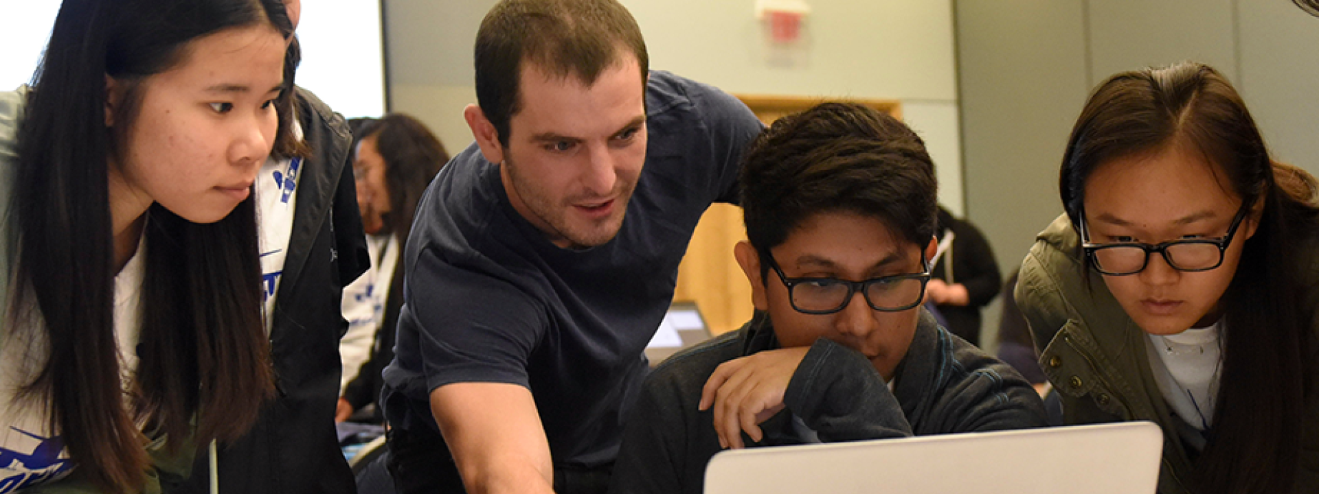 students gaze at laptop with teacher