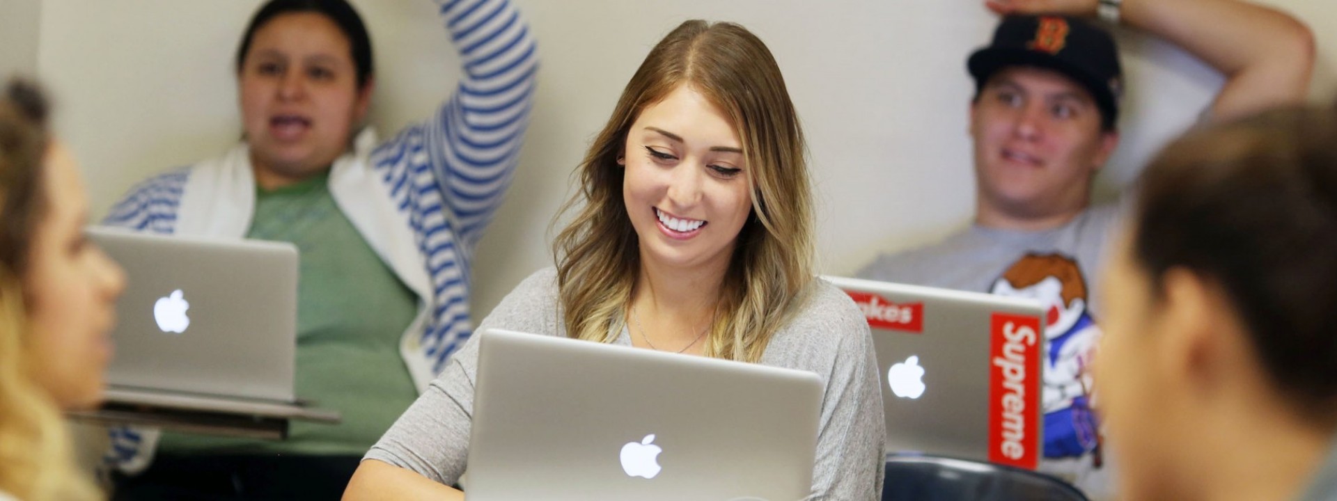 Image of a Caucasian female student smiling in a classroom setting in front of an open laptop. 