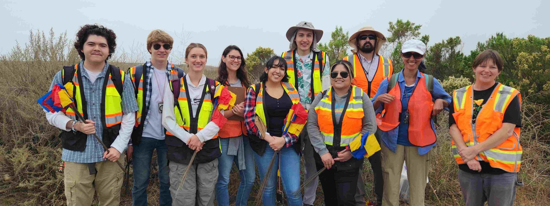Group wearing safety vests smiling in front of the coastline.
