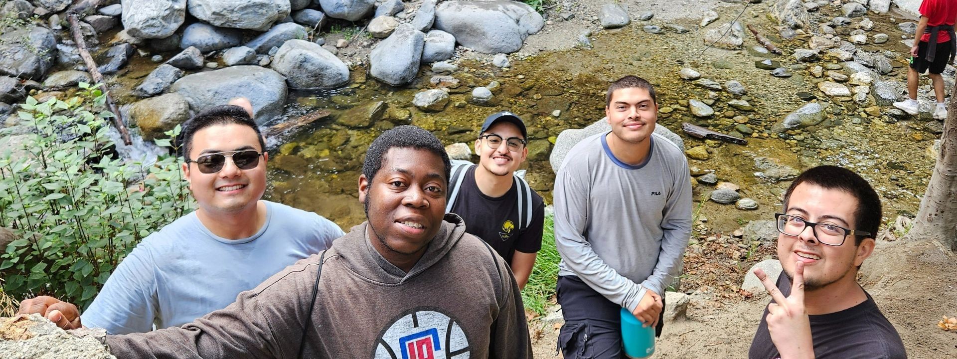 5 Men smiling in front of a stream of water and boulders.