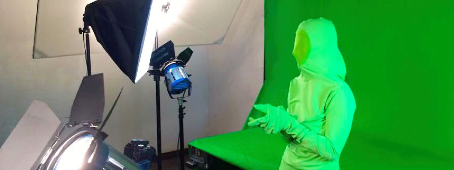 Image of a student in a green suit in front of a green screen being filmed. 