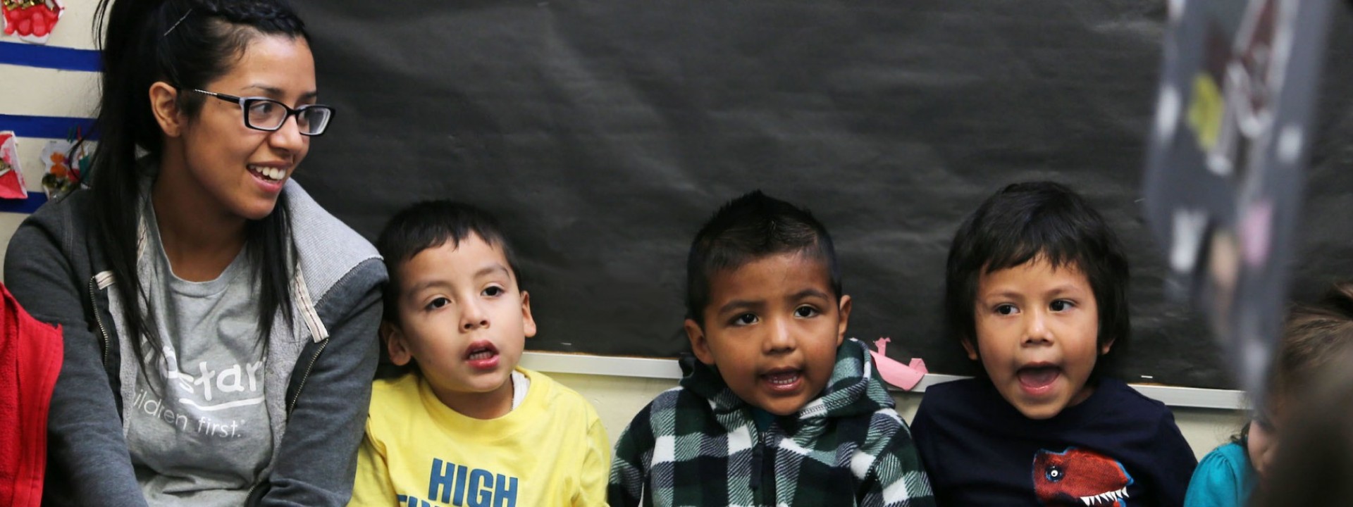 Image of a Cal State LA female student sitting next to three small children who appear to be singing. 