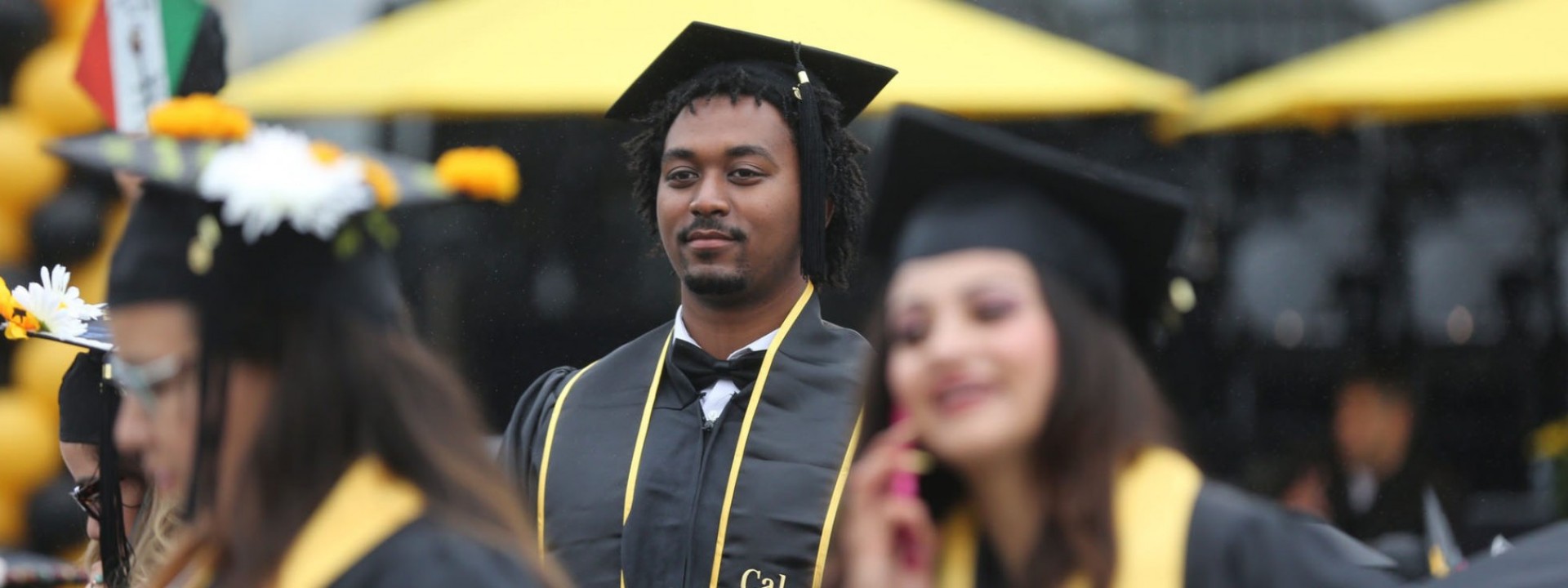 Image of a Black male student in Commencement regalia with a stoic expression on his face. 