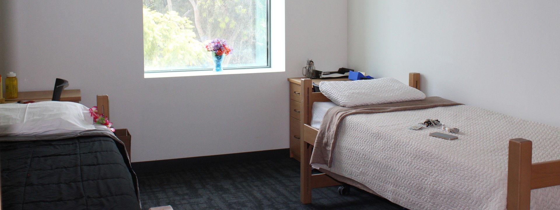 Room with two beds, keys and other small objects are on one bed, a small vase with flowers is on the window.