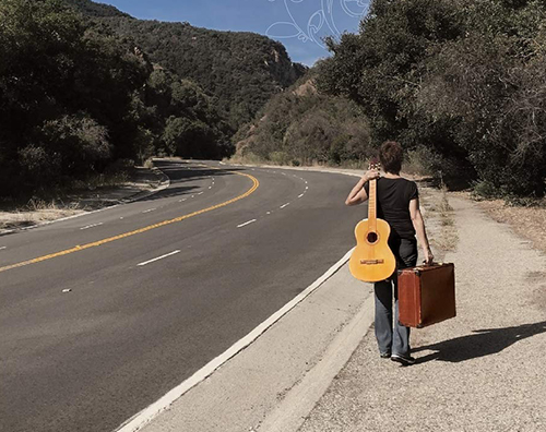 A woman walking down the street with a guitar