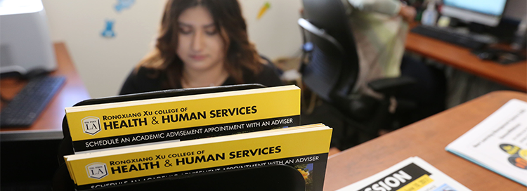 Student working in the HHS advising center with flyers on the front desk. 